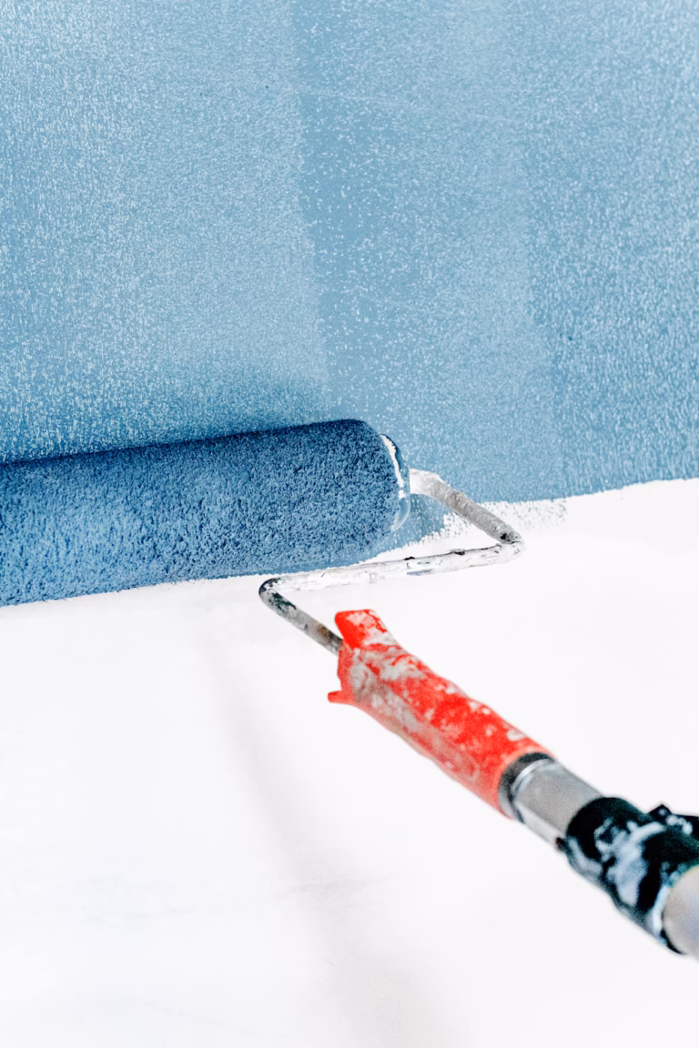 Paint roller applying fresh blue emulsion paint