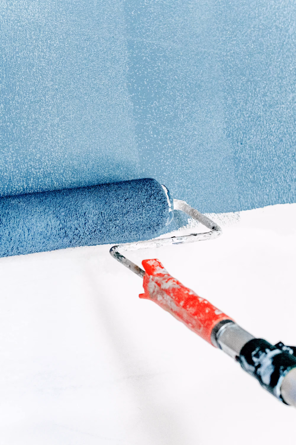 Paint roller applying fresh blue emulsion paint